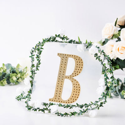 Gold letter "B" surrounded by greenery and white flowers on a clear backdrop.