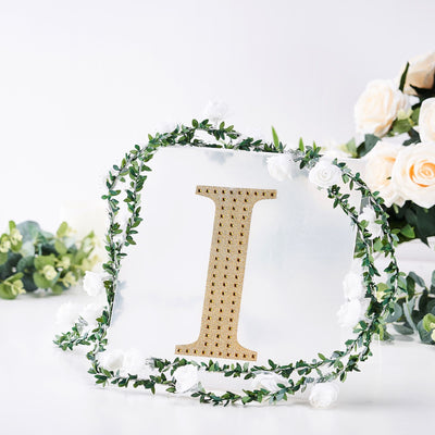 Gold letter "I" surrounded by greenery and flowers on a white background