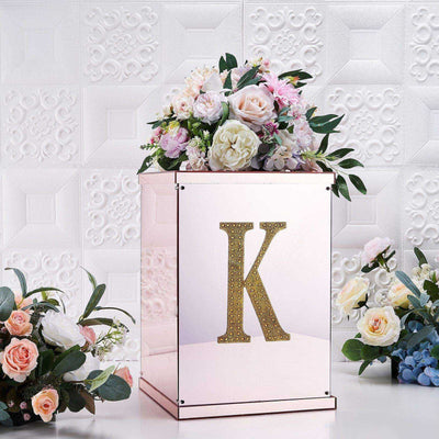 Rose gold floral display box with a golden letter "K" and assorted flowers.