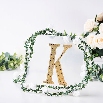 Gold letter "K" surrounded by floral greenery and white roses.