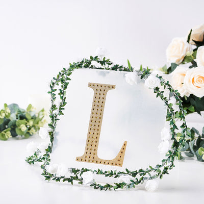 Decorative letter "L" surrounded by greenery and white flowers on a reflective surface.