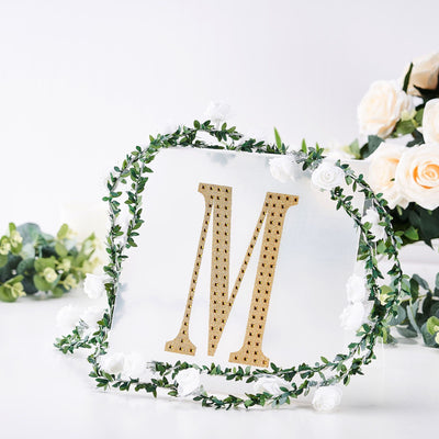 Gold letter "M" decor surrounded by floral accents on a clear backdrop.