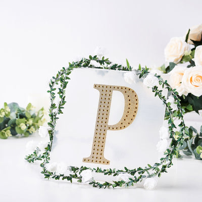 Gold letter "P" surrounded by greenery and white flowers on a clear backdrop.