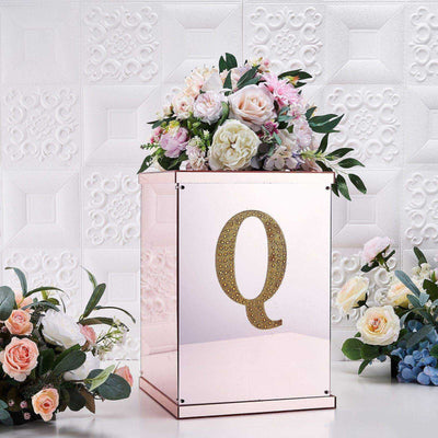 Rose gold gift box with floral arrangement and letter "Q" on a textured background.