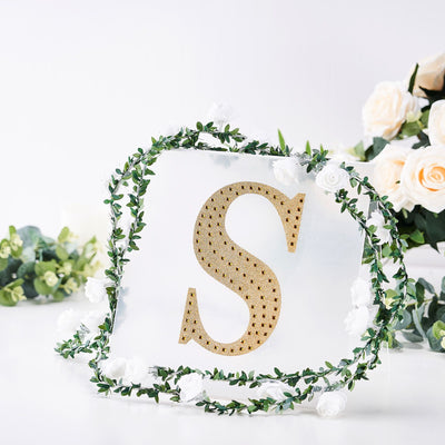 Gold letter "S" surrounded by white flowers and greenery decor.