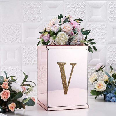 Decorative floral arrangement in a mirrored vase with a gold letter "V" accent.