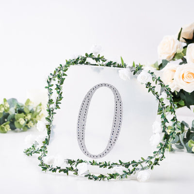 Silver number "0" surrounded by floral decoration on a white backdrop.
