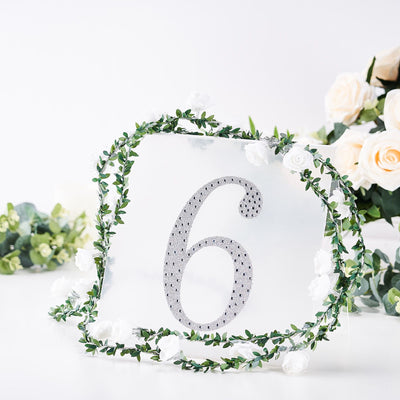 Decorative table number 6 with rhinestones and floral accents on a white backdrop.