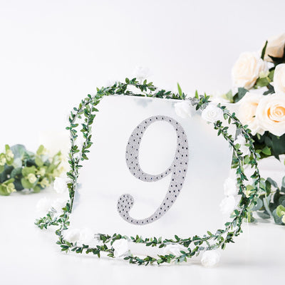Silver glitter number 9 surrounded by floral decor on a white backdrop.