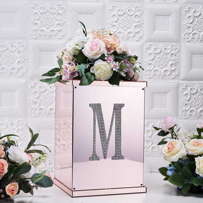 Rose gold floral arrangement box with decorative letter "M" and flowers.