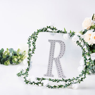 Decorative letter "R" adorned with flowers and greenery on a white background.