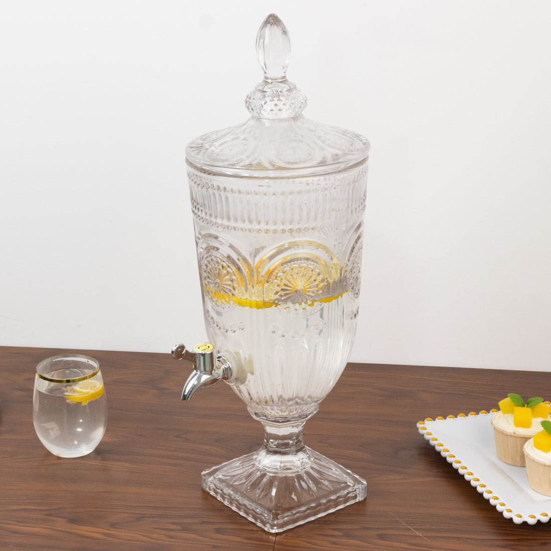 Vintage glass beverage dispenser with ornate design and lemon slices.