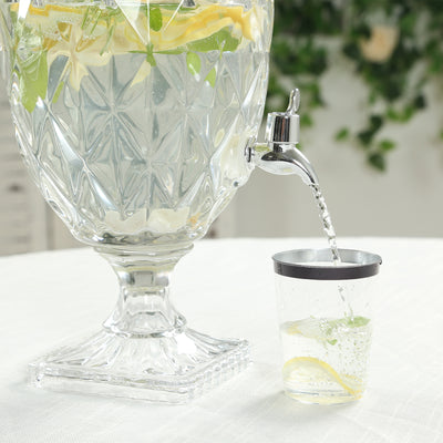 Glass beverage dispenser with lemon and mint-infused water pouring into a cup.