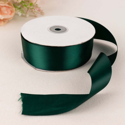Green satin ribbon roll with loose end on a plain background.