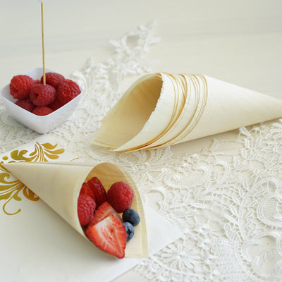 Cone-shaped dessert cups with fresh berries on a lace tablecloth.
