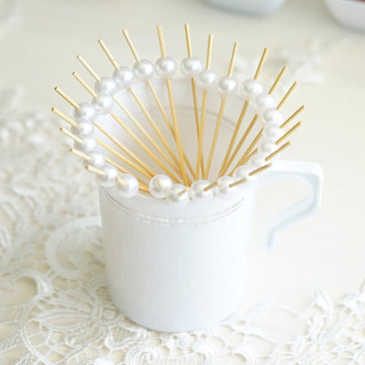 White mug with pearl-tipped skewers arranged decoratively inside.