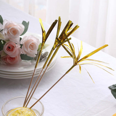 Gold foil decorative picks in a glass with flowers on a table.
