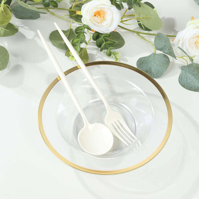 Clear glass bowl with gold rim and white utensils on a light background.