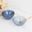 Set of elegant blue bowls with gold trim and a golden spoon on a marble surface.