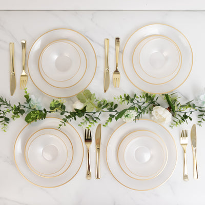 Elegant table setting with gold-accented plates and cutlery, adorned with greenery.