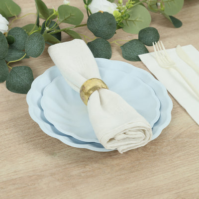 Blue scalloped plates with a napkin and gold napkin ring, styled with greenery.