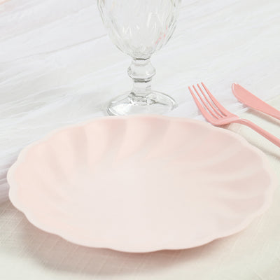 Pink scalloped plate with a glass and cutlery on a textured tablecloth.