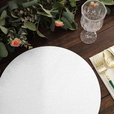 Round silver table charger on a wooden table with floral accents and glassware.