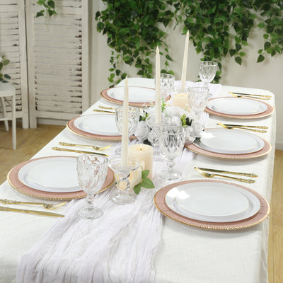 Elegant dining table set with gold-accented plates and candles, surrounded by greenery.