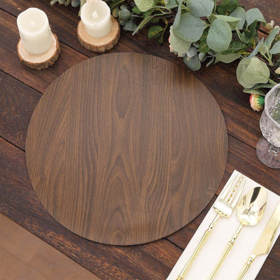 Round wooden placemat on a rustic table with candles and greenery.