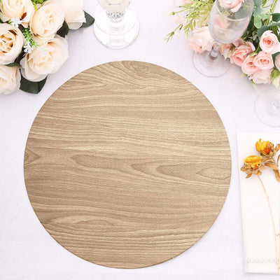 Round wooden placemat on a decorated dining table with flowers and glassware.