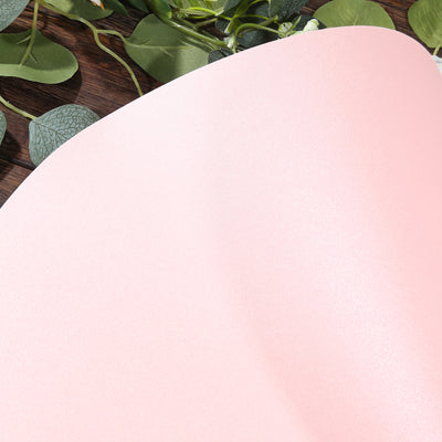 Pink textured paper with a subtle shimmer against a wooden backdrop.