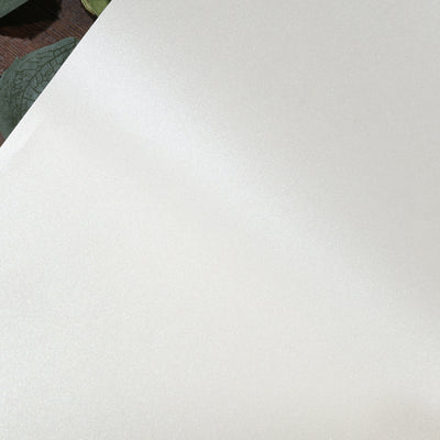 Shiny cream fabric swatch on a wooden surface with green leaves.