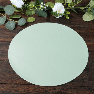 Green circular placemat on a wooden table with foliage and flowers around it.