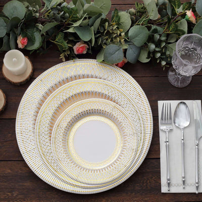 Elegant gold-trimmed dinnerware set on rustic wooden table with greenery.