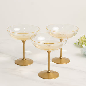 Set of three elegant gold-rimmed champagne coupes on a marble surface.