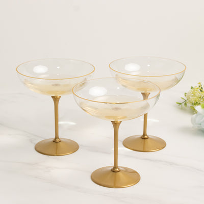 Set of three elegant gold-rimmed champagne coupes on a marble surface.
