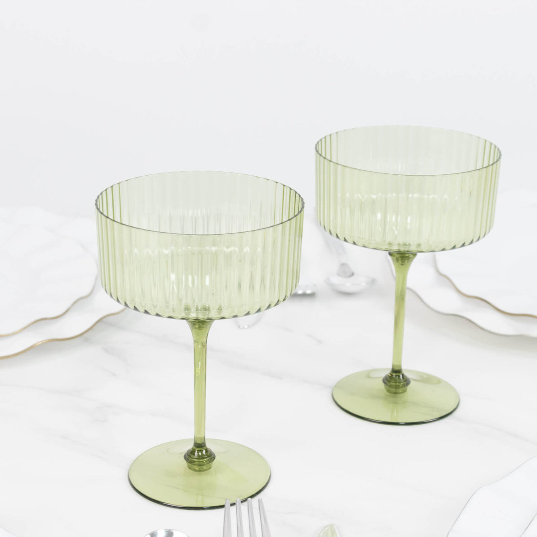 Two green ribbed coupe glasses on a white marble table.