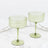 Two green ribbed coupe glasses on a white marble table.