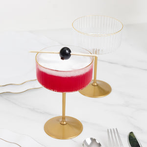 Elegant cocktail glasses with red drink and black garnish on a marble countertop.