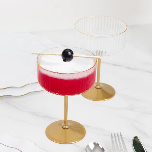 Elegant cocktail glasses with red drink and black garnish on a marble countertop.