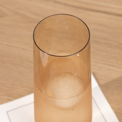 Transparent amber glass with ice on a wooden surface.