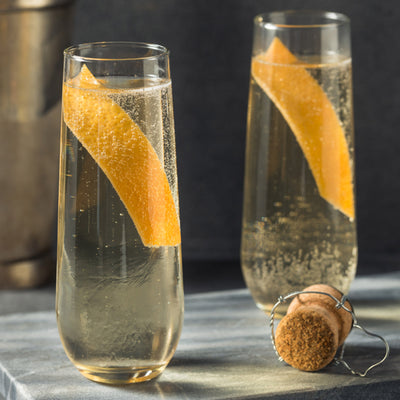 Two elegant champagne flutes with orange twists and a cork on a marble surface.