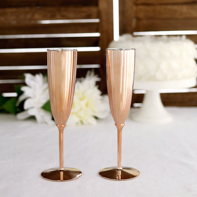 Rose gold champagne flutes on a table with floral decor in the background.