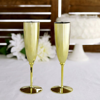 Gold champagne flutes set on a table with a cake in the background.
