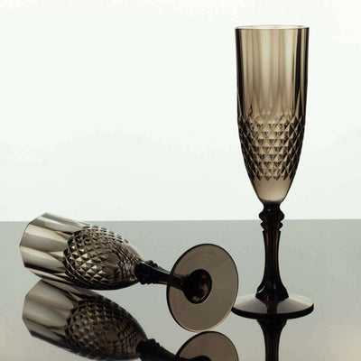 Elegant crystal champagne flutes in smoky gray, one upright and one tipped over.