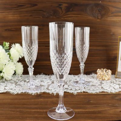 Elegant crystal champagne flutes set on a wooden table with lace and flowers.