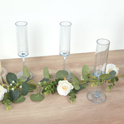 Three elegant blue champagne flutes with greenery and roses on a wooden surface.