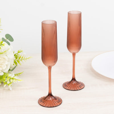 Two rose gold ribbed champagne flutes on a white table, elegant stemware set