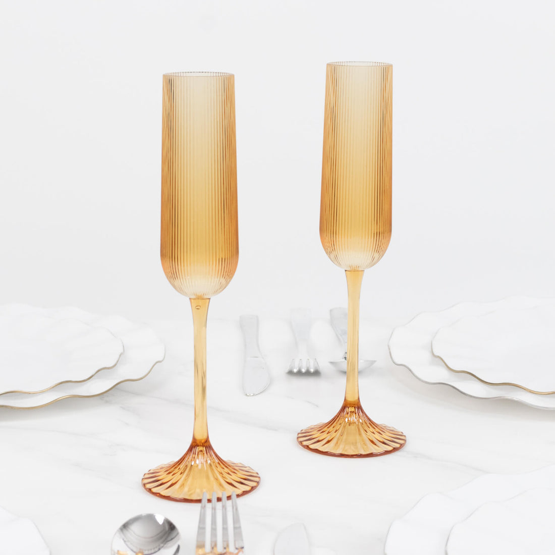 Amber ribbed champagne flutes with gold stems on white marble table
