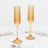Amber ribbed champagne flutes with gold stems on white marble table
